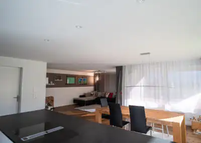 Moderne, offene Wohnküche mit Esstisch, schwarzem Herd und gemütlicher Sitzecke im Sonnenlicht.