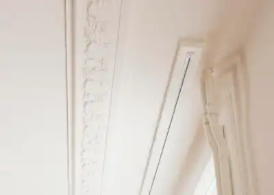 Ornamentierte Stuckdecke mit eleganten Verzierungen neben modernen Vorhangschienen an einem Fenster.