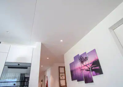 Moderne Küche mit Blick auf abgehängte Decke, integrierter Beleuchtung und Wandkunst mit lila Naturmotiv.