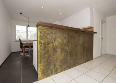 Moderne Küche mit goldener Akzentwand, Holztisch und stilvollen schwarzen Stühlen im Essbereich.