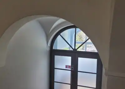 Weiße Bogenarchitektur über Glastür mit Sicht nach draußen, Tageslicht erhellt den Raum.