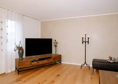 Modernes Wohnzimmer mit Holzboden, großem Flachbild-TV und minimalistischer Dekoration auf einem Holzmöbelstück.