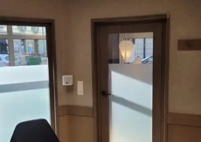Büroeingang mit Glastür und Milchglas, daneben ein Fenster mit Sicht auf die Straße. Moderne Innenarchitektur.