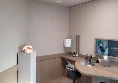Moderner Hörgeräteraum mit Laptop, Ohrmodell und Display an der Wand, passend für Beratungs- und Anpassungsdienste.
