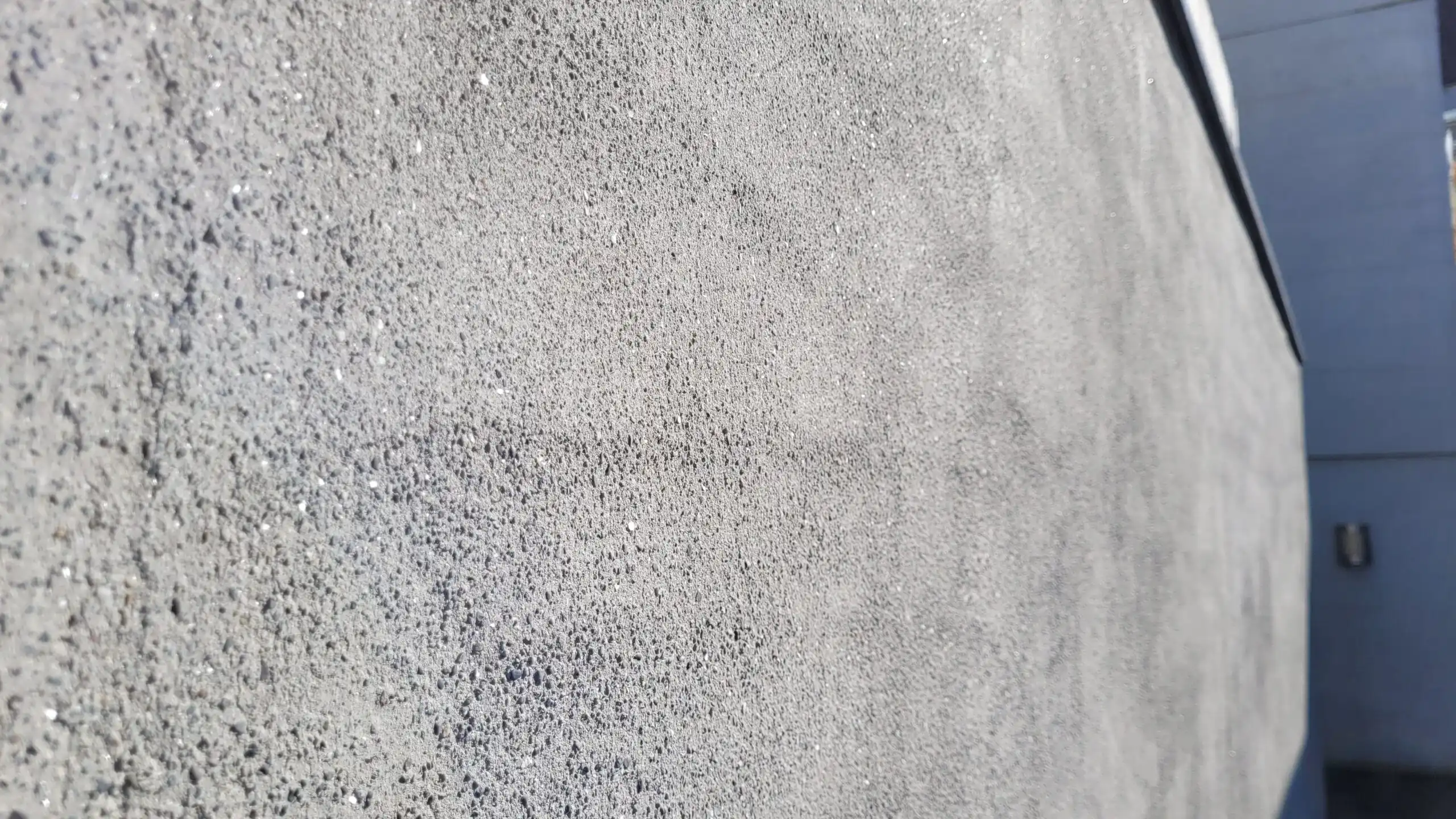 Grau strukturierte Betonwand mit unregelmäßiger Oberflächenstruktur in Nahaufnahme unter Tageslicht.