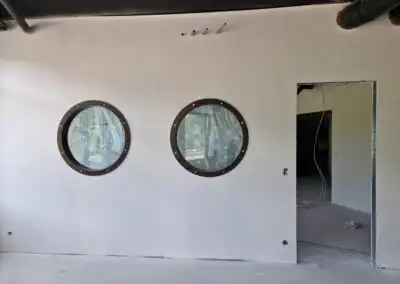 Zwei runde Fenster und eine Türöffnung in einer weißen Wand eines Gebäudes im Bau.