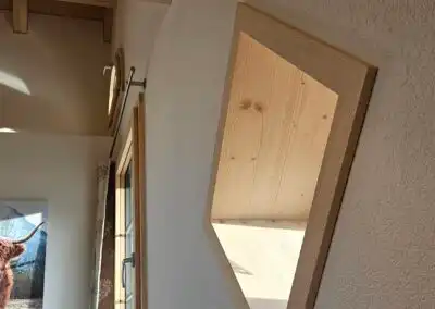 Holzwand und schräger Spiegel in rustikalem Raum mit Tageslicht, moderner Dekoration und Holzbalken.