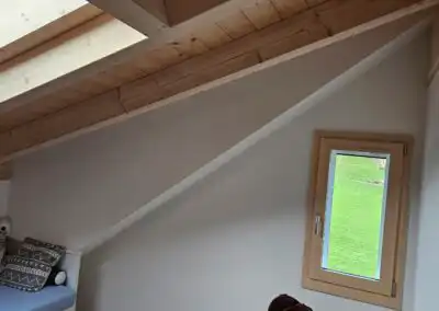 Dachzimmer mit Holzdecke, Fenster und Sofa mit Kissen, bietet gemütliche und helle Atmosphäre.