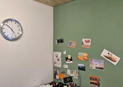 Wanduhr auf weißer Wand und Pinnwand mit Karten und Fotos auf grüner Wand im Büro oder Zuhause.