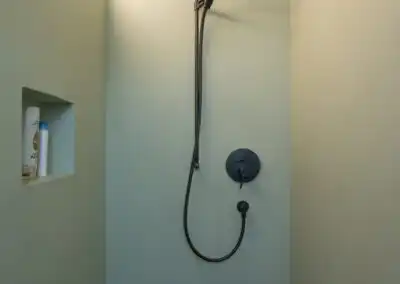 Moderne Dusche mit Regenduschkopf und eingebautem Regal an mintgrüner Wand. Minimalistisches Design.