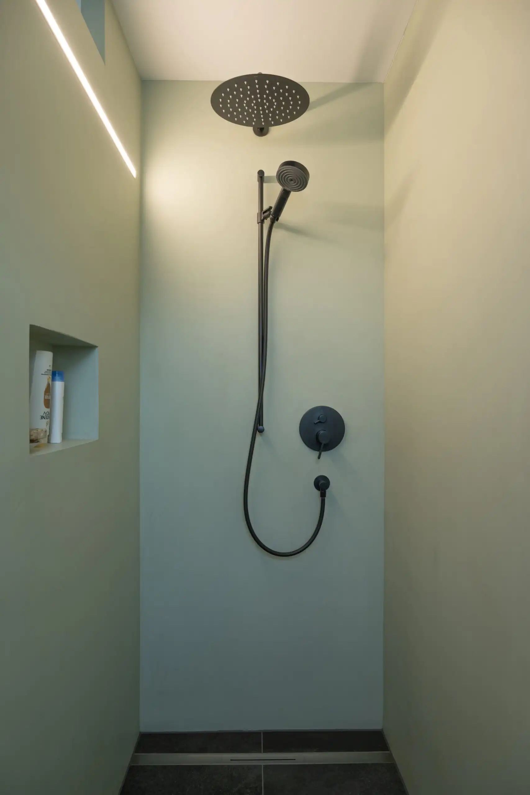 Moderne Dusche mit Regenduschkopf und eingebautem Regal an mintgrüner Wand. Minimalistisches Design.