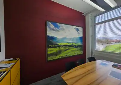 Büro mit roter Wand, beeindruckendem Landschaftsgemälde, großem Fenster und Holztisch für kreatives Arbeiten und Meetings.