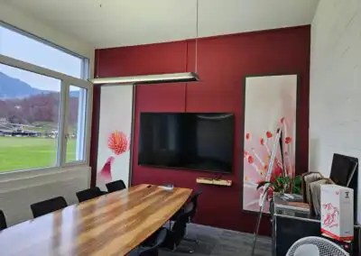 Moderner Konferenzraum mit großem Tisch, Flachbildschirm und Blick auf grüne Landschaft durch Fenster.