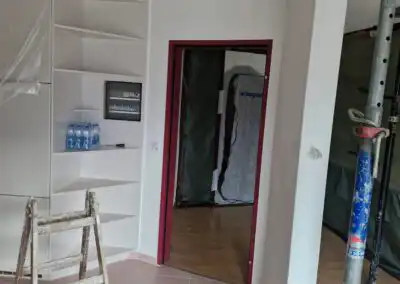 Renovierung in einem Wohnraum mit Leiter, Fliesenboden und Türrahmen in Rot. Werkzeuge für Innenausbau sichtbar.