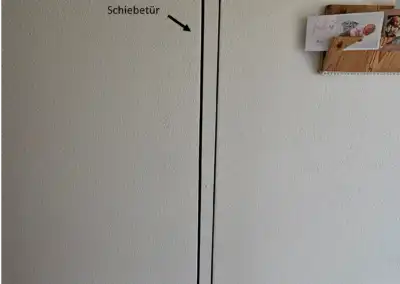 Schiebetür an weißer Wand mit Postkartenhalter aus Holz und neugeborenen Babybildern, Beschriftung zeigt auf Tür.
