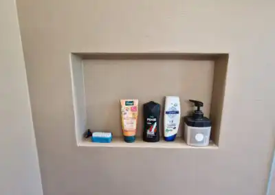 Duschprodukte in Wandnische: Shampoo, Duschgel, Lotion und Seifenspender auf beiger Fliese, platzsparend arrangiert.