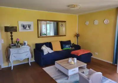 Gemütliches Wohnzimmer mit gelber Wand, blauer Couch, dekorativer Kommode und Wandspiegel, ideal zum Entspannen.