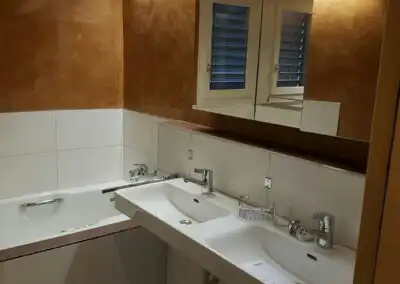 Modernes Badezimmer mit Doppelwaschbecken, Badewanne und stilvollen braunen Wänden sowie Spiegel über dem Waschbecken.