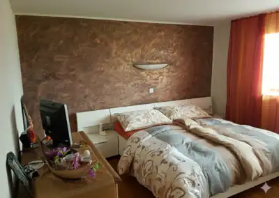 Gemütliches Schlafzimmer mit floralem Bettzeug, brauner Akzentwand und dekorativem Tisch mit Vase.