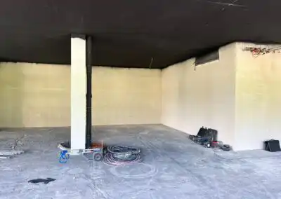 Leerer Raum mit weißen Wänden, schwarzer Decke und Kabelrollen auf Betonboden. Baustelle, Renovierung oder Lagerung.