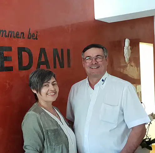 Paar lächelt vor einem roten Wandhintergrund mit „EDANI“-Schriftzug.