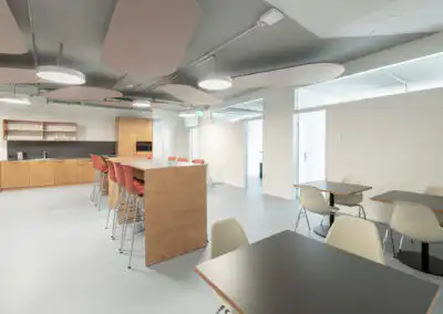 Moderne Büroküche mit hohen Tischen und Stühlen, ausgestattet mit Küchengeräten und hellem Interieurdesign.