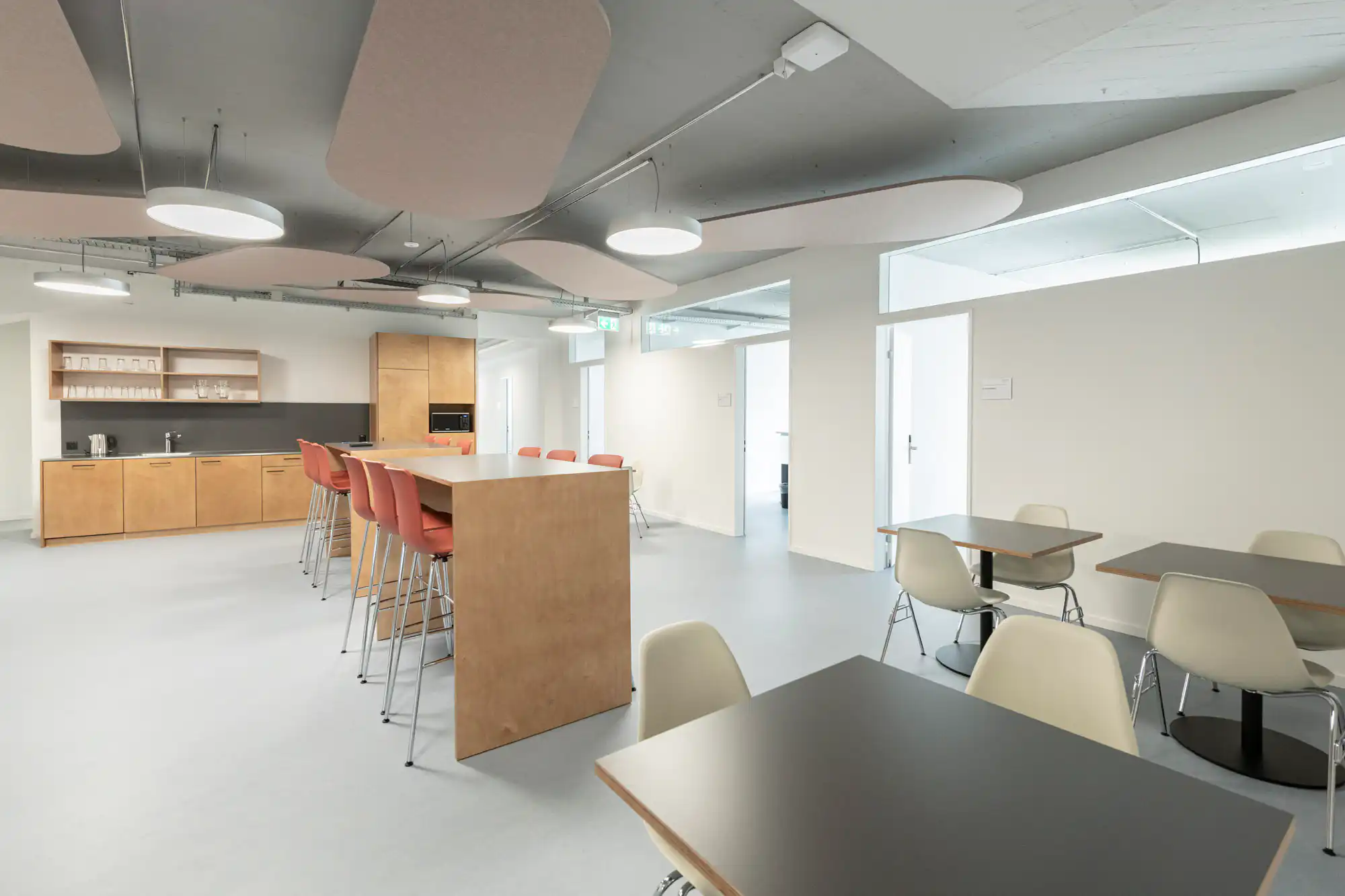 Moderne Büroküche mit hohen Tischen und Stühlen, ausgestattet mit Küchengeräten und hellem Interieurdesign.
